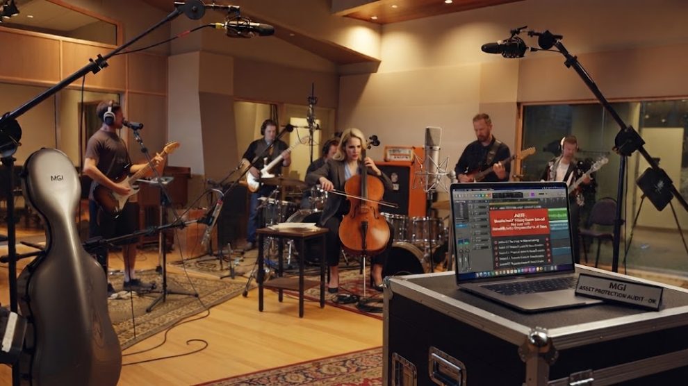 Blonde string player and independent instrumentalists tracking multitrack audio in a professional recording studio, auditing digital stems for AI training protection.